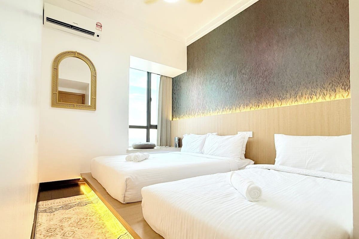 Habitació d'hotel amb dos llits, un mirall gran i una finestra amb cortines.