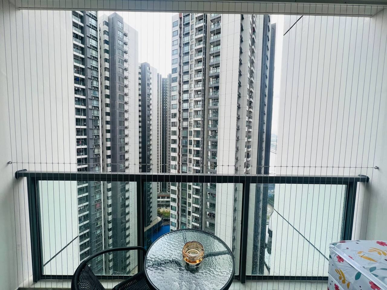 Un balcón con una mesa de vidrio y una silla, con vistas a edificios altos.