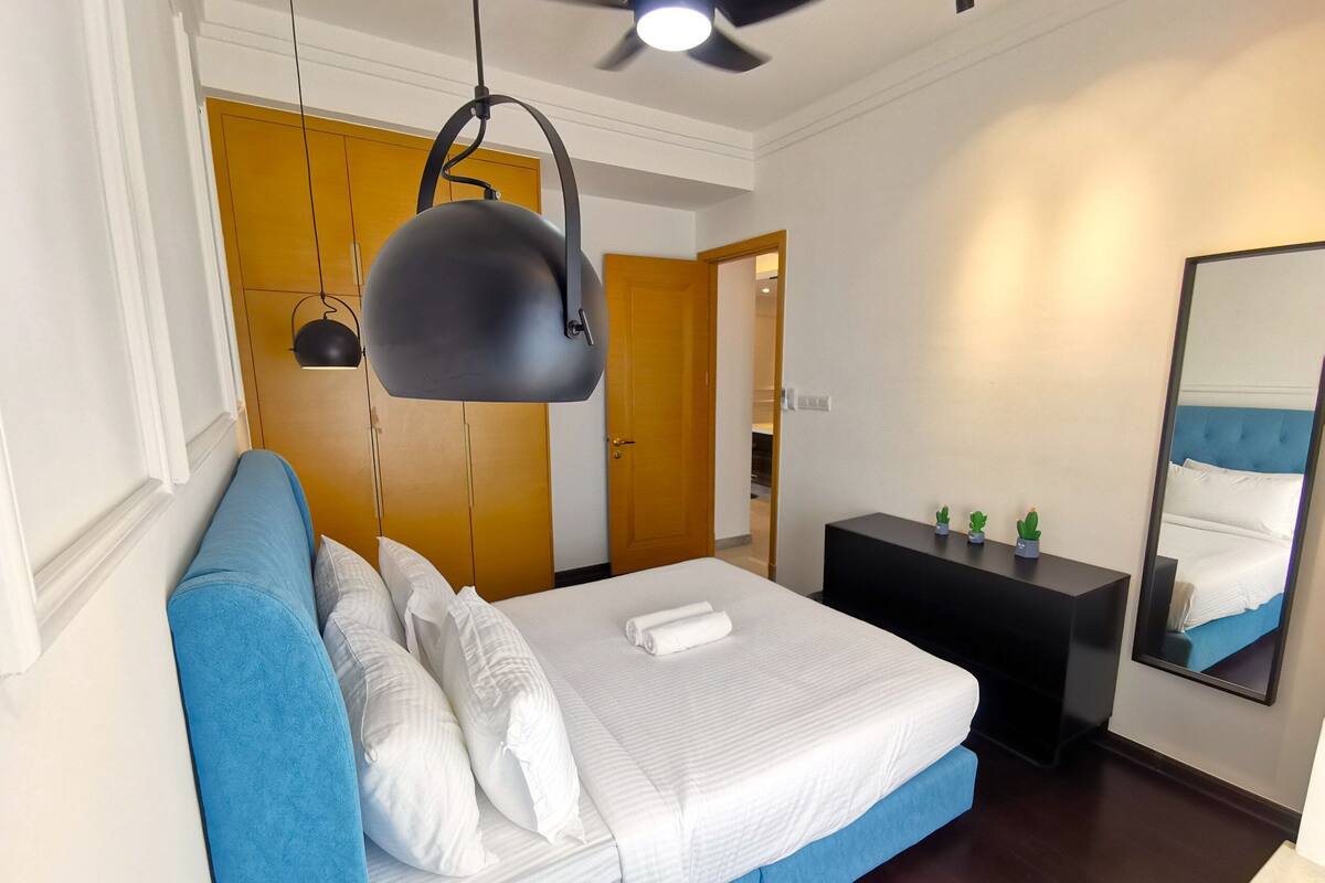 Habitació d'hotel moderna amb un llit gran, un sofà blau, un escriptori petit i un ventilador de sostre.