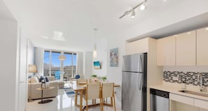 A modern kitchen with a stainless steel refrigerator, a dining area with a table and chairs, and a large window offering a city view. - Spectacular Balcony View Retreat: Resort Amenities (Hallandale Beach)