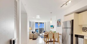 A modern kitchen with a stainless steel refrigerator, a dining area with a table and chairs, and a view of the city through large windows. - Spectacular Balcony View Retreat: Resort Amenities (Hallandale Beach)