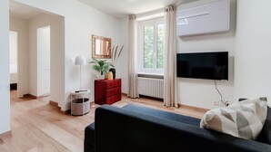 Una sala moderna con televisor de pantalla plana, un mueble rojo, una lámpara de pie y un ventanal con cortinas.