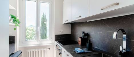 A modern kitchen with white cabinets, a black marble countertop, and a window with a view of trees.