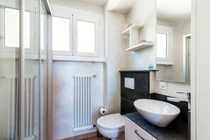 Bathroom features a glass shower enclosure, white toilet, and shelf.
