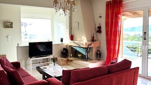 Un salón con sofá rojo, televisor, chimenea y vistas al exterior.