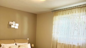 Un dormitorio ordenado con cama, almohadas, una mesita de noche y una ventana con cortinas.