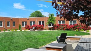 A courtyard with a brick building, green lawn, wooden deck, and outdoor seating area. - The West End Flats (Roanoke)