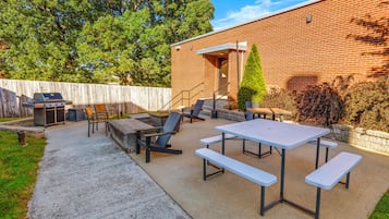 An outdoor patio with a barbecue grill, seating area, and a brick building in the background.