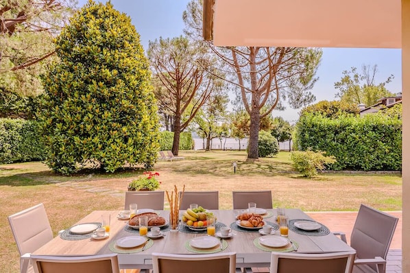 An outdoor dining area with a table set for breakfast, surrounded by greenery and trees. - Large lakeside villa (Lesa)