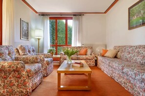 A living room with floral-patterned sofas, a wooden coffee table, and a window with curtains.