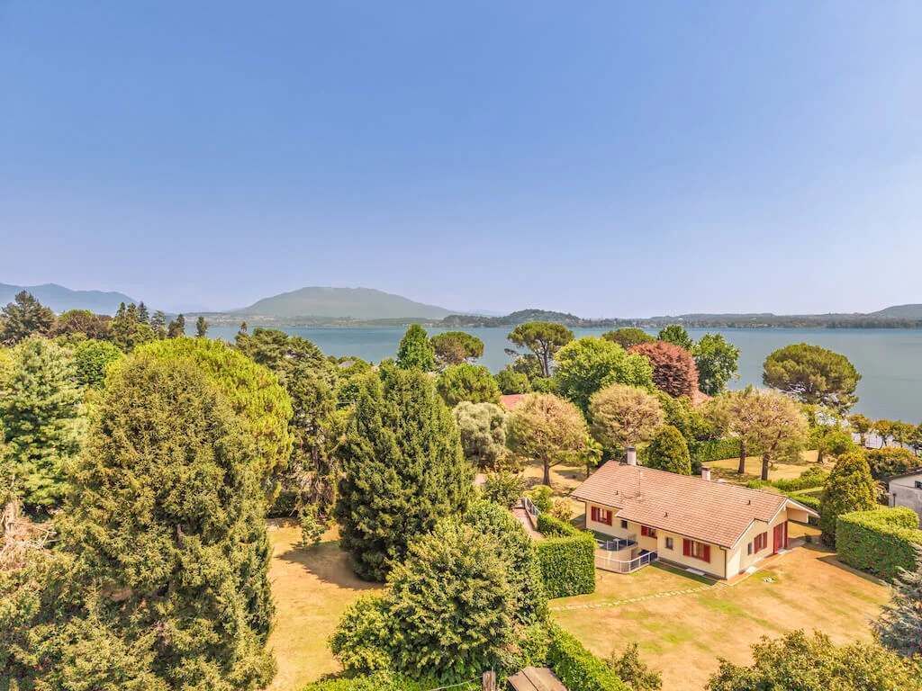 Propiedad residencial con una casa rodeada de abundante vegetación y un lago al fondo.