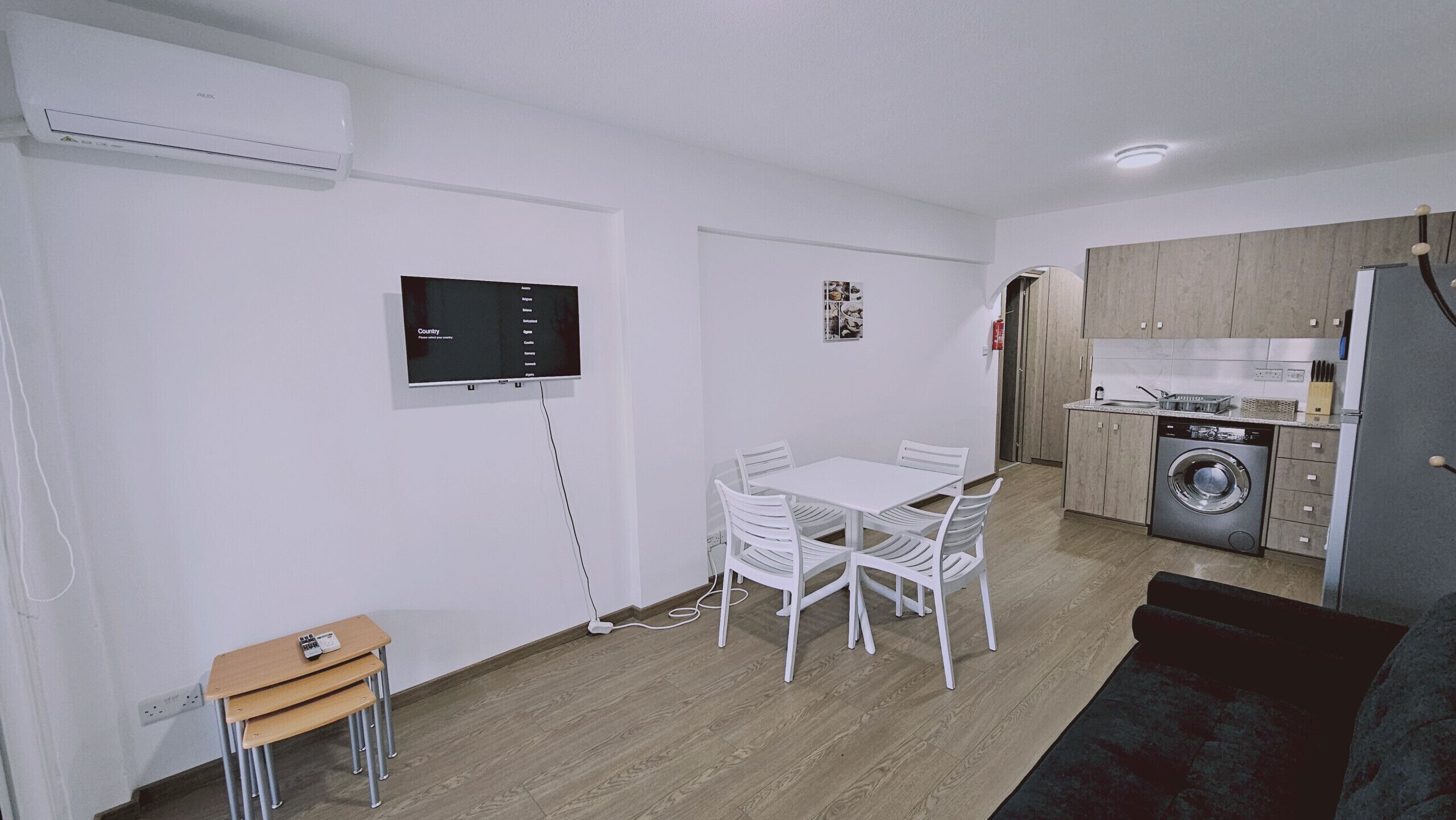 Un espace de vie compact comprenant un coin repas, une kitchenette et un téléviseur fixé au mur.