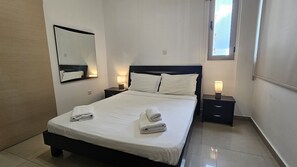 Habitación de hotel con cama, dos mesitas de noche, un tocador, un espejo y una ventana.