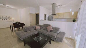 Una sala moderna con un sofá seccional gris, una mesa de comedor con sillas y una cocina con armarios y un refrigerador.