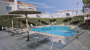 A swimming pool with lounge chairs and umbrellas, surrounded by a hedge and buildings. - STAY White Petals Apartment (Larnaca)