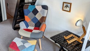 Ein Sessel mit Patchwork-Sitzfläche und passendem Hocker, ein schwarzer Metalltisch mit Lampe und ein gerahmtes Bild an der Wand.