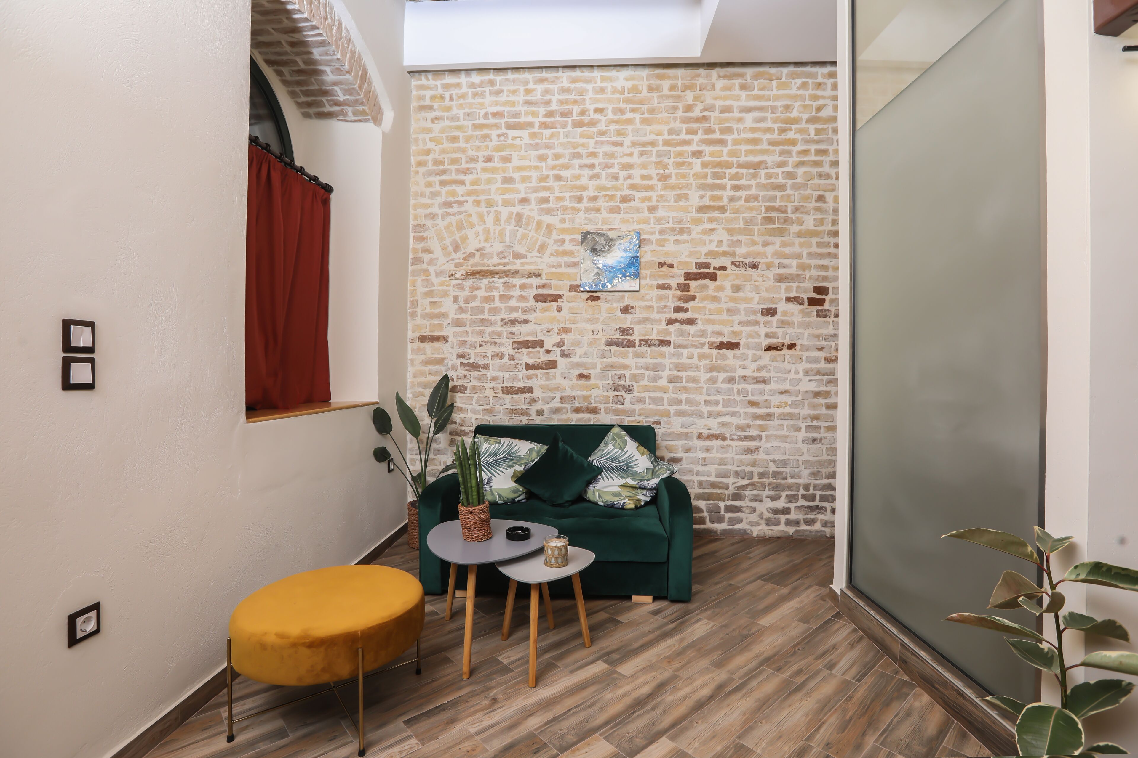 A cozy room with a brick wall, a green sofa, a small round table, and a yellow ottoman.