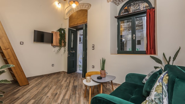 Un salon chaleureux avec un plancher en bois, un canapé vert, une petite table ronde et un téléviseur fixé au mur.