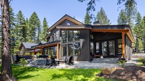 Una casa moderna con ventanas amplias, un porche cubierto y un entorno de bosque natural.