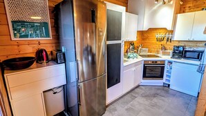 A compact kitchen with wooden beams, a stainless steel refrigerator, white cabinets, and a tiled floor. - Le Beaulieu Chalet (Beaulieu)