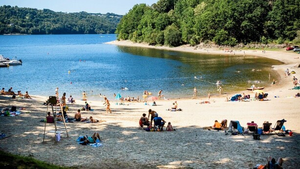 A beach with people sunbathing and swimming, surrounded by trees and a clear sky. - Le Beaulieu Chalet (Beaulieu)