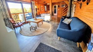 A cozy wooden cabin interior with a sofa, a coffee table, and a dining table. - Le Beaulieu Chalet (Beaulieu)