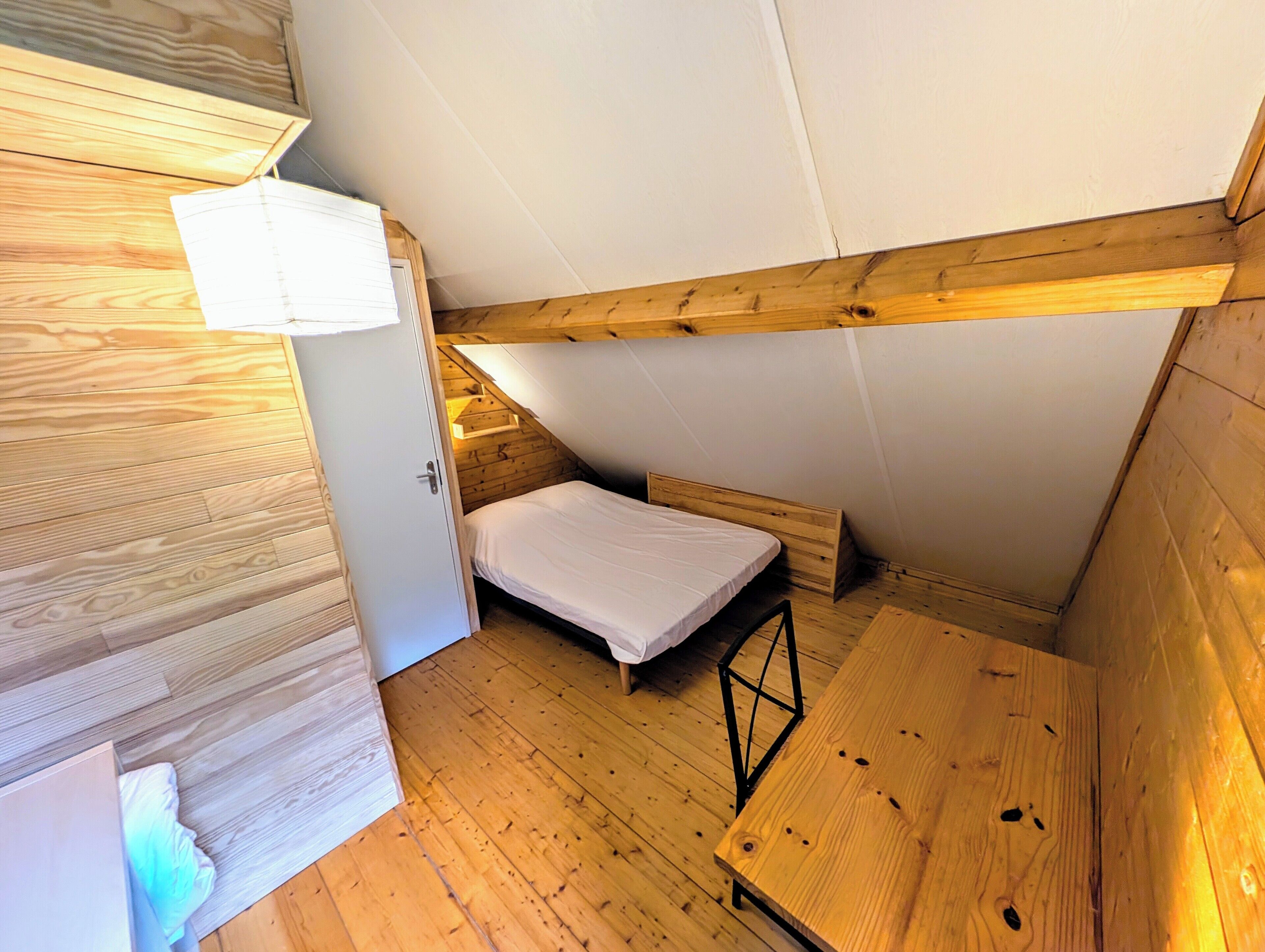 A small, wooden room with a bunk bed, a wooden table, and a door.