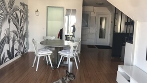 A dining area with a round table and white chairs, a staircase leading to another level, and a dog sitting on a rug.