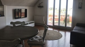 A room with a dining table, chairs, a TV mounted on the wall, a radiator, and a large sliding glass door leading to an outdoor area.