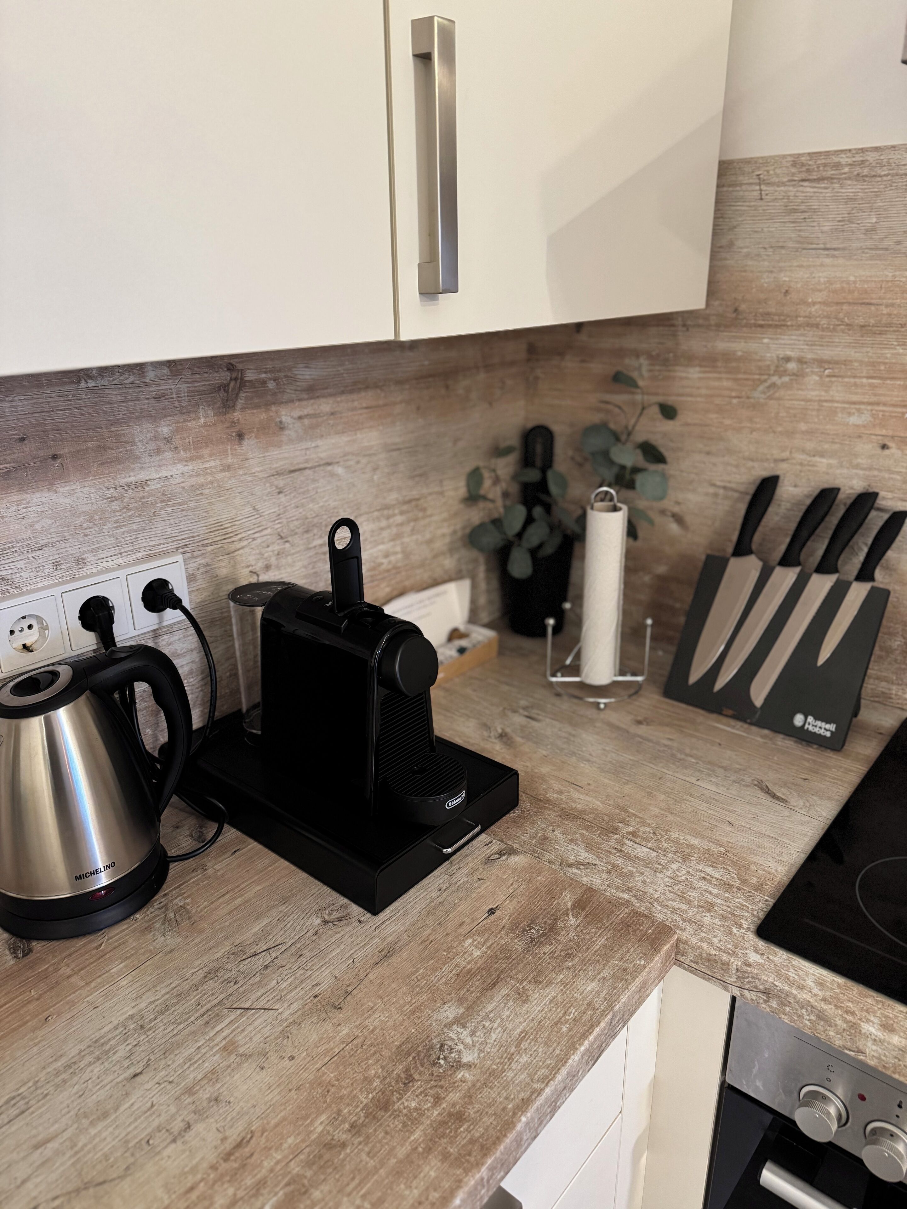 Una cocina con cafetera, hervidor y juego de cuchillos sobre una encimera de madera.