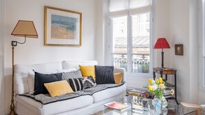 A living room with a white sofa, a glass coffee table, and a red lamp. - Honeybee Soul, by Veeve (Paris)