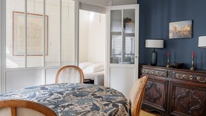 A bedroom with a bed, a dresser, a chair, and a window with blinds. - Honeybee Soul, by Veeve (Paris)