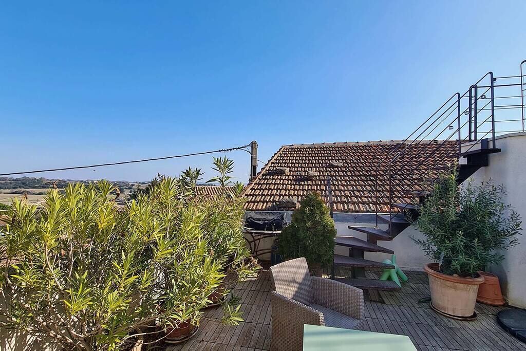 Terraza en la azotea con techo de tejas, mobiliario exterior y plantas en macetas.