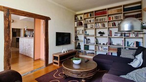 Een woonkamer met een grote boekenkast, een ronde houten salontafel en een bank.