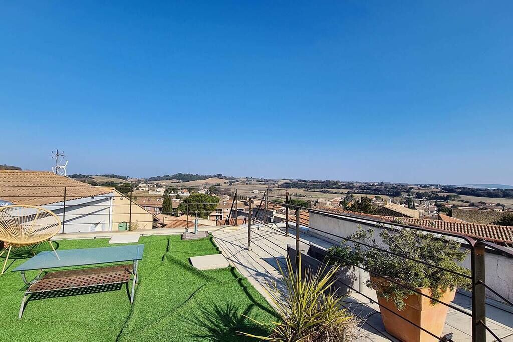 A rooftop terrace with a green artificial lawn, a metal table, and a potted plant.
