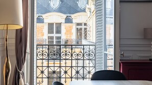A room with a dining table, chairs, a lamp, and a view of a building through a window with curtains. - Clichy Couture, by Veeve (Paris)