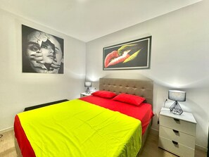 Une chambre à coucher comprenant un lit, une table de chevet, une lampe et deux œuvres d’art accrochées au mur.