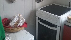 Een keuken met een fornuis, oven, hangende pannen en een plank met potten.