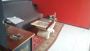 Een kamer met een grijze bank, een klein houten tafeltje met een dienblad, een rode muur en een tapijt met een patroon.