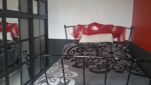 Een eenpersoonsbed met een beddekleed met patroon, een rode hoofdbord en een zwart metalen frame.