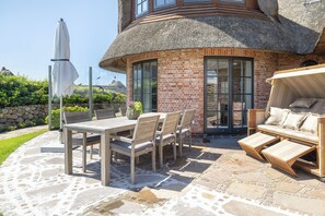 Une terrasse avec une table et des chaises, un canapé et un bâtiment dont le toit est fait de chaume.
