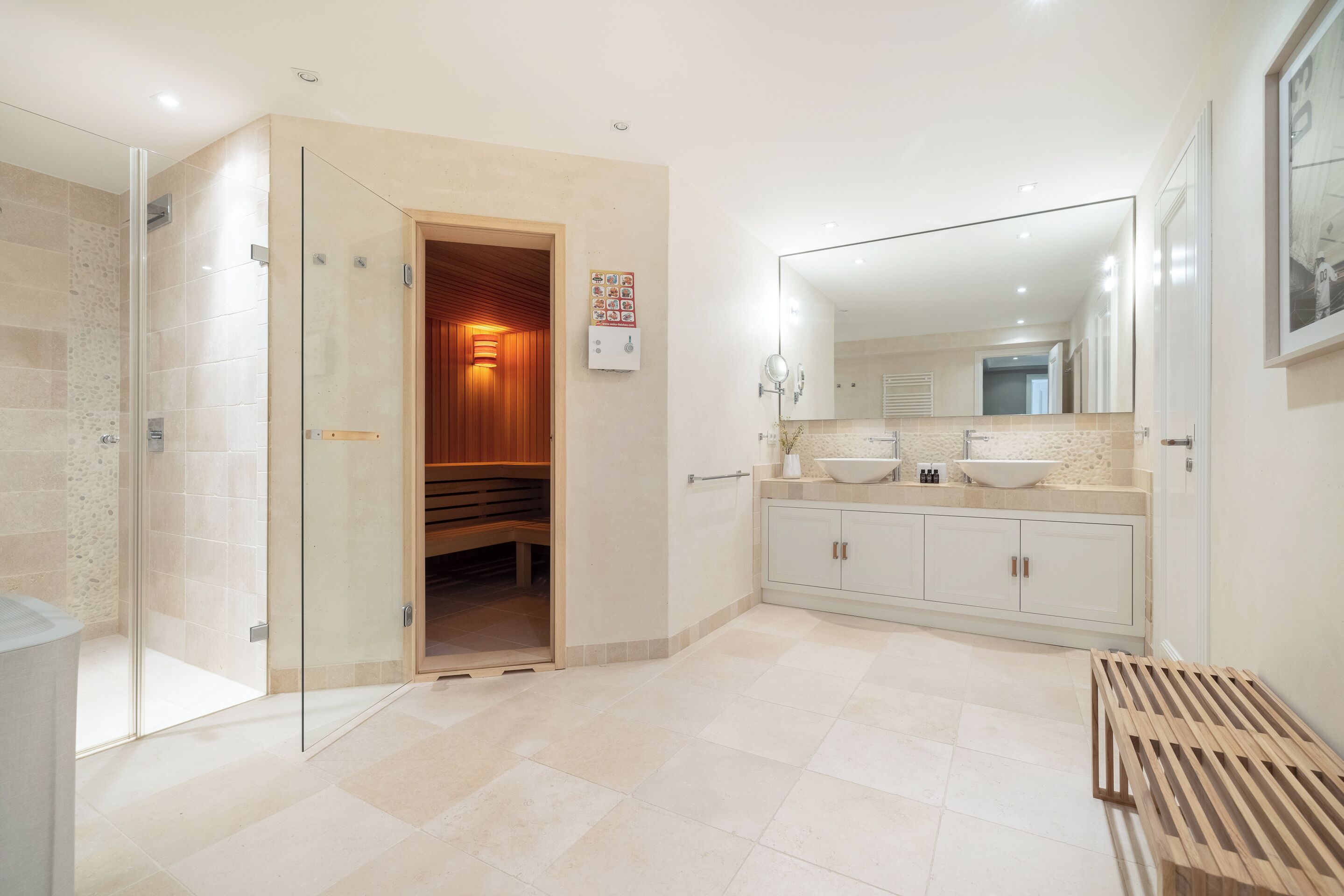 Une salle de bain moderne dotée d’une douche à parois de verre, d’un banc en bois, d’un grand miroir et d’un meuble-lavabo avec un évier et un placard.