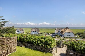 Un paysage rural avec des maisons aux toits de chaume, un mur de pierre et une vue sur la mer.