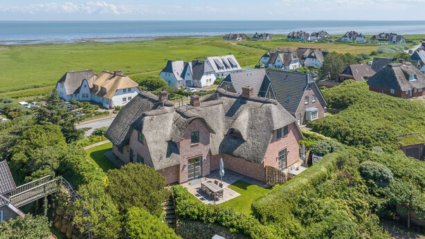 Un village côtier aux maisons traditionnelles, avec un bâtiment central doté d’un grand patio et offrant une vue sur la mer.