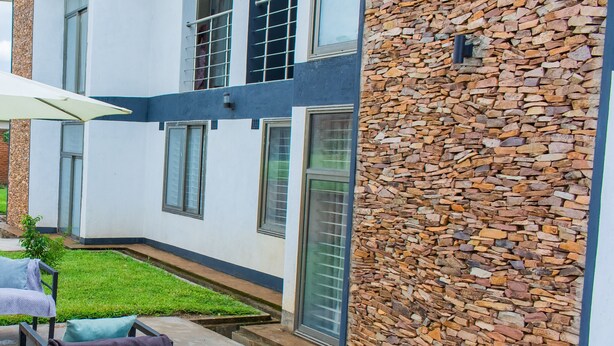 Un edificio moderno con fachada de piedra, un pequeño césped y mesas al aire libre.