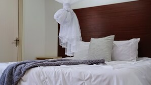 Una cama bien hecha con ropa de cama blanca, un edredón de punto gris y un dosel blanco.