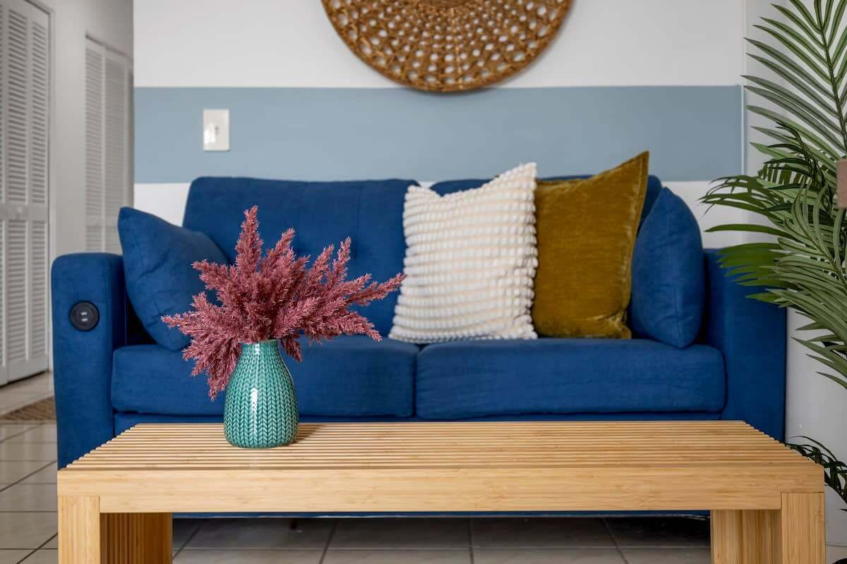 Un sofá azul con un jarrón verde y una mesa de centro de madera.