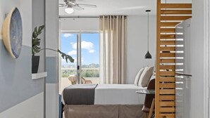 Een slaapkamer met een bed, een raam met gordijnen, een plafondventilator en uitzicht op de omgeving.