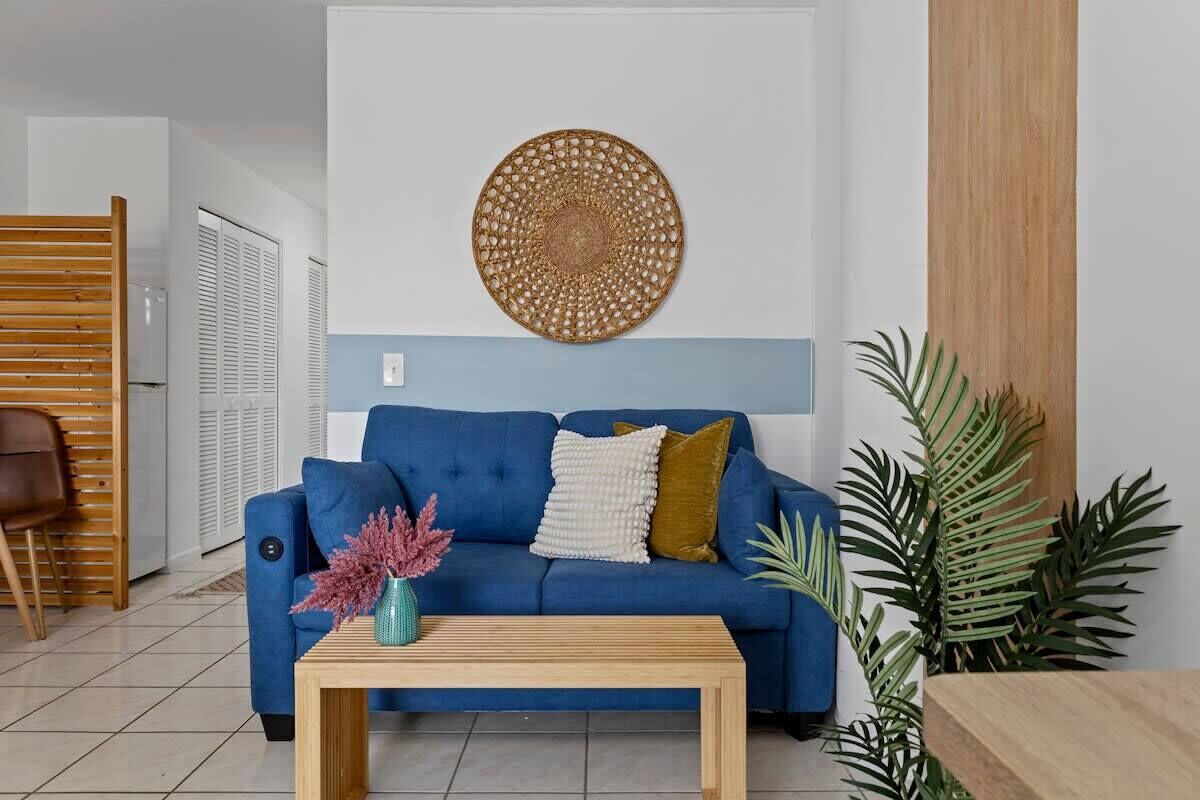Ein Wohnzimmer mit einem blauen Sofa, einem Holztisch und einer Wanddekoration.