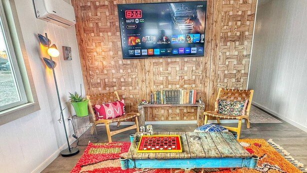Un salon moderne avec un grand téléviseur à écran plat fixé sur un mur en bois, un coin salon confortable agrémenté d’un tapis coloré et une bibliothèque remplie de livres.
